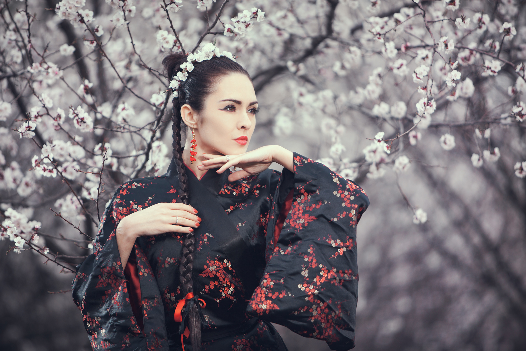 Attractive asian woman wearing kimono standing in blossoming garden. Gorgeous creative portrait outdoor on the nature. Girl looking away